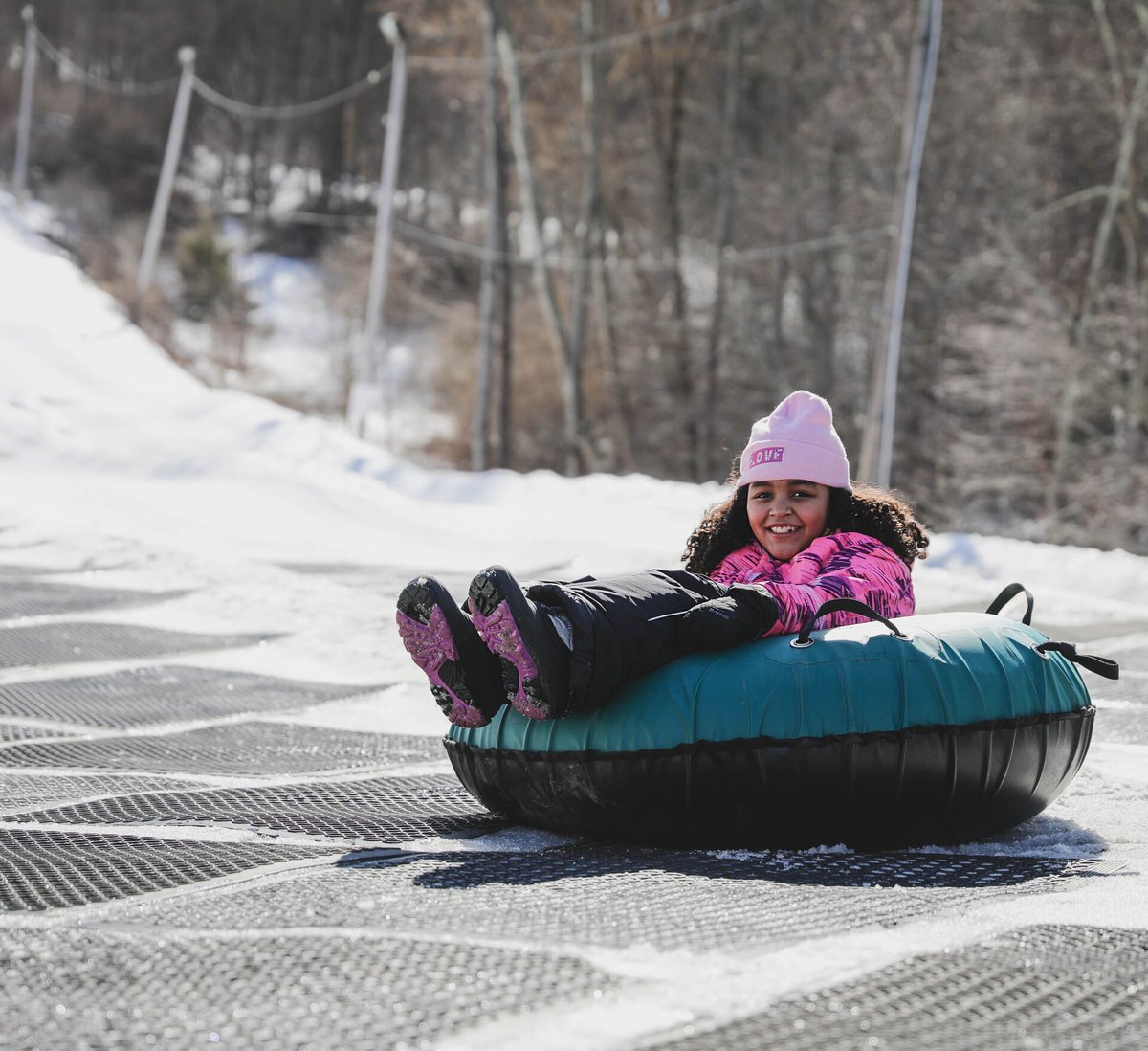 Young girl in pink coat in a blue and black snow tube on tubing field trip