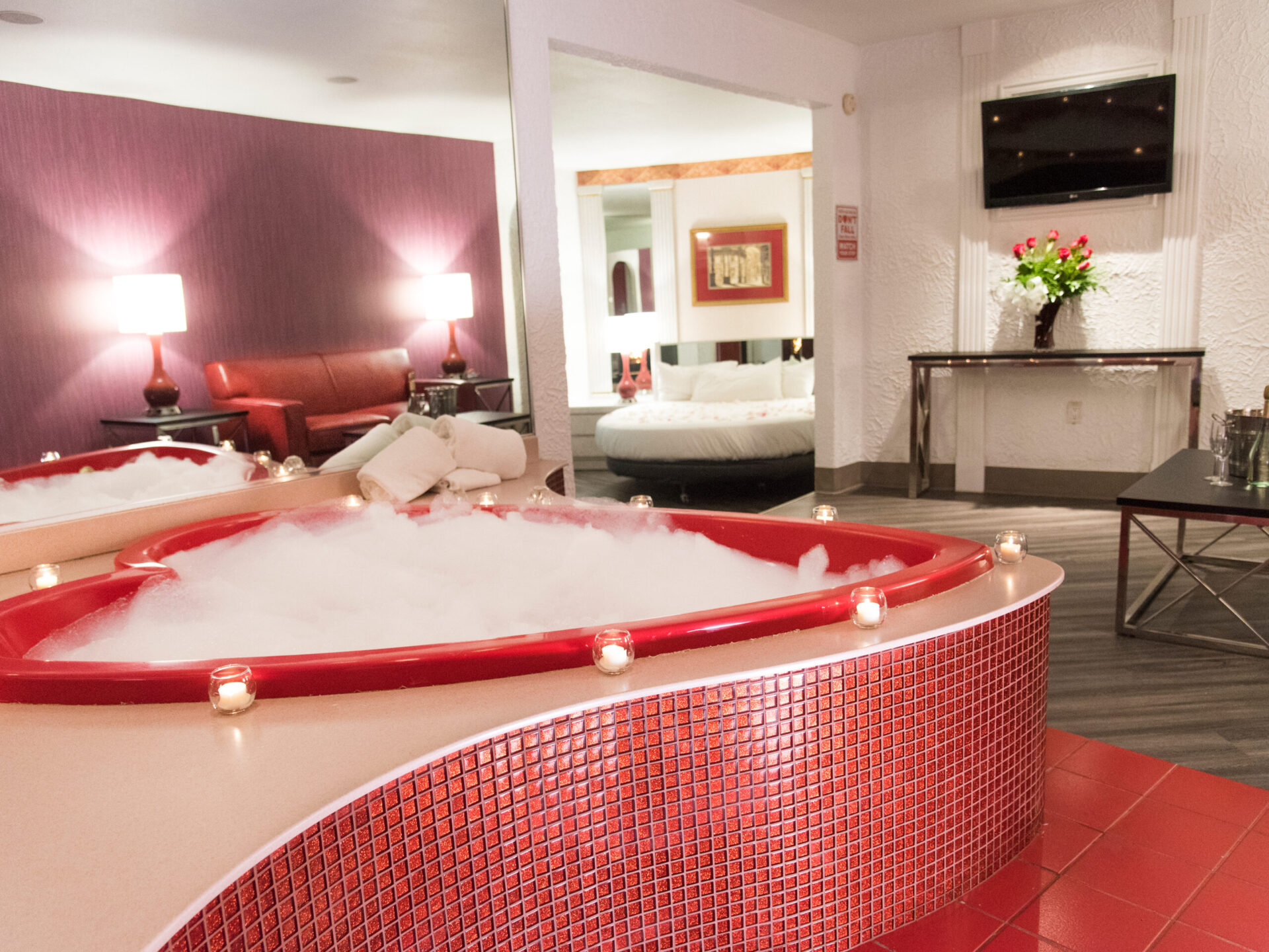 A hotel room with a red heart shaped tub surrounded by candles.