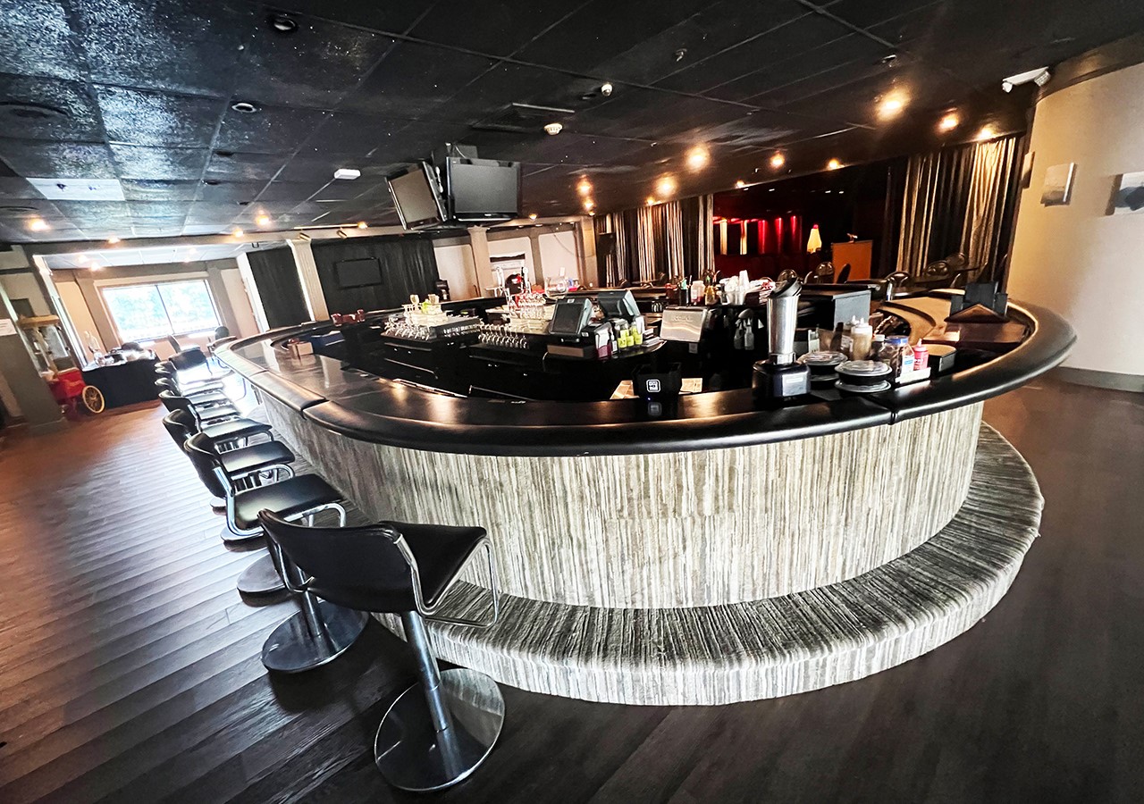 Wide shot of an oval grey and black colored bar with multiple bar stools